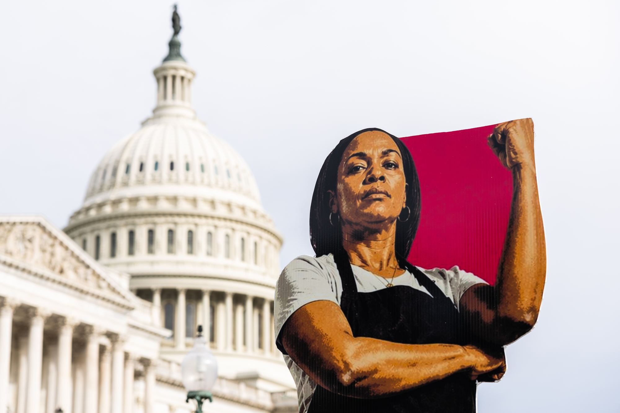 A large cutout portrait of a worker with her fist raised, in front of the U.S. Capitol