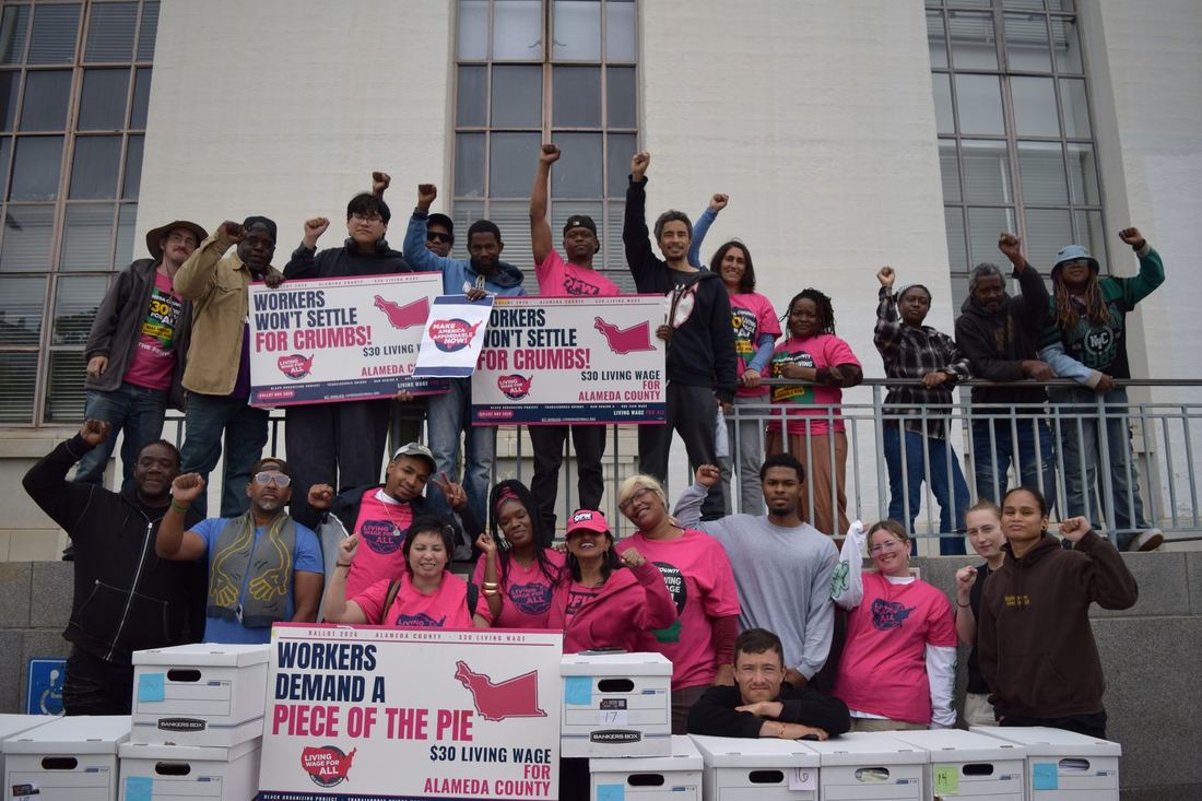Workers celebrating beside boxes of signatures for the Alameda County living wage measure